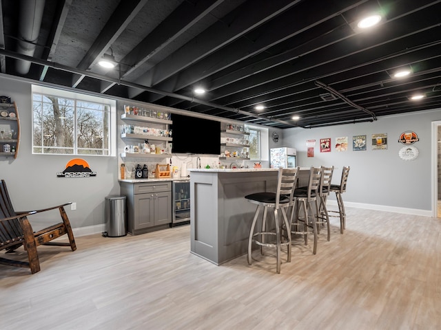 bar featuring light wood finished floors, baseboards, wine cooler, and bar area