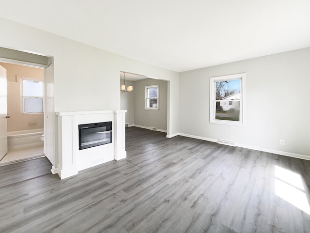unfurnished living room featuring a glass covered fireplace, visible vents, baseboards, and dark wood finished floors