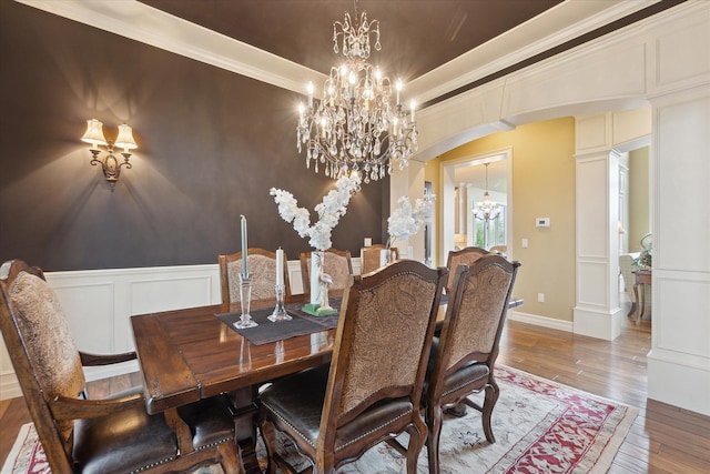 dining room featuring a chandelier, arched walkways, hardwood / wood-style floors, a decorative wall, and wainscoting