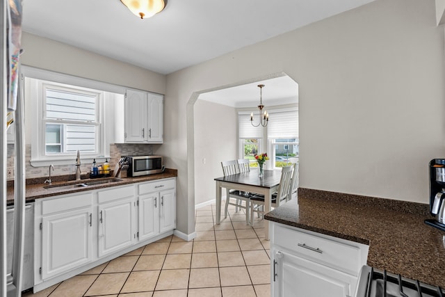 kitchen with a sink, appliances with stainless steel finishes, white cabinetry, a chandelier, and light tile patterned floors