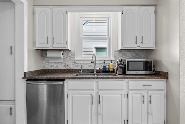 kitchen featuring stainless steel appliances, a sink, dark countertops, and white cabinetry