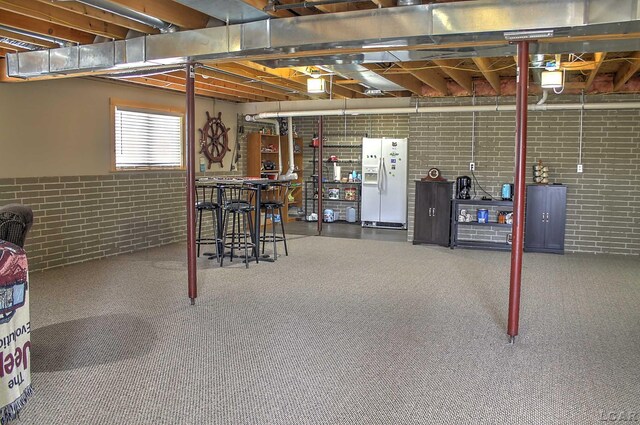 below grade area with white fridge with ice dispenser, carpet flooring, brick wall, and wainscoting