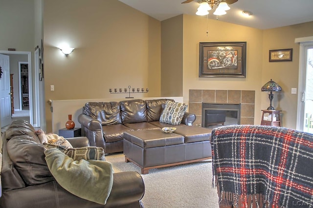 living area featuring vaulted ceiling, a tiled fireplace, a ceiling fan, and carpet
