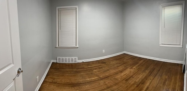 spare room featuring dark wood-style flooring, visible vents, and baseboards