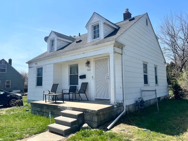 back of property with a chimney, a lawn, a shingled roof, and covered porch