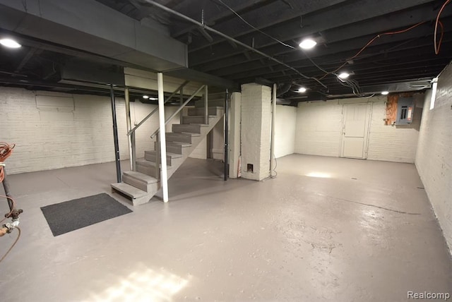 unfinished basement featuring brick wall, electric panel, and stairway