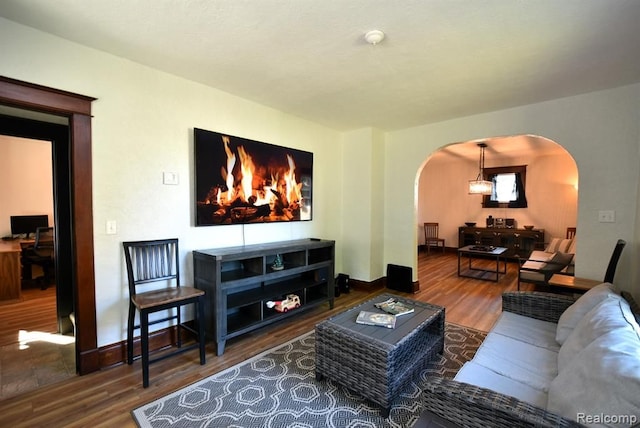 living area featuring arched walkways, wood finished floors, and baseboards