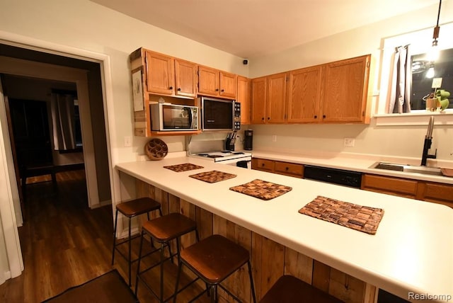 kitchen featuring a sink, light countertops, a breakfast bar, dark wood finished floors, and black appliances