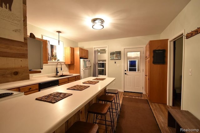 kitchen with a sink, light countertops, freestanding refrigerator, a kitchen breakfast bar, and dishwashing machine
