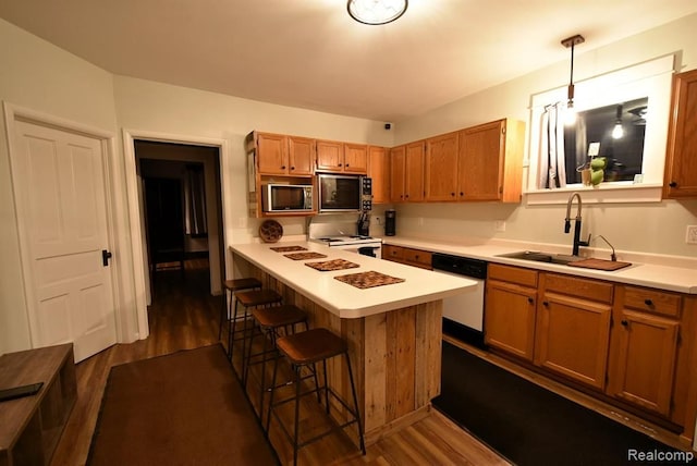 kitchen featuring a sink, dark wood-style flooring, light countertops, a kitchen breakfast bar, and white appliances