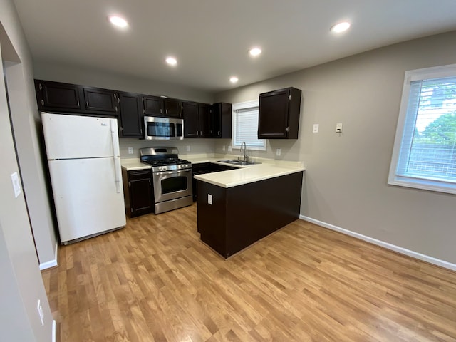 kitchen with a peninsula, light wood-type flooring, light countertops, dark cabinetry, and appliances with stainless steel finishes