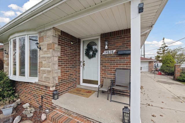 view of exterior entry with brick siding, fence, and covered porch