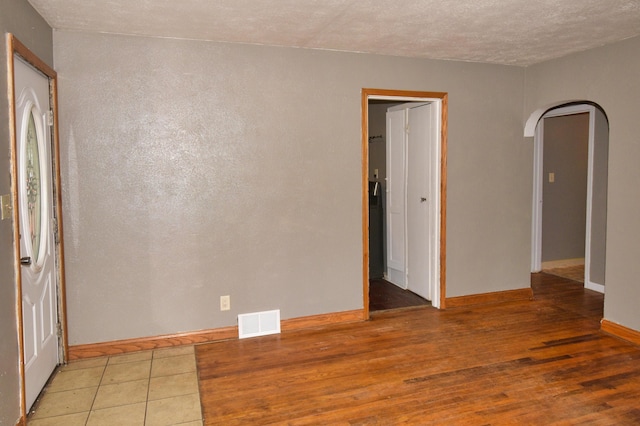 unfurnished room with arched walkways, wood finished floors, baseboards, and visible vents
