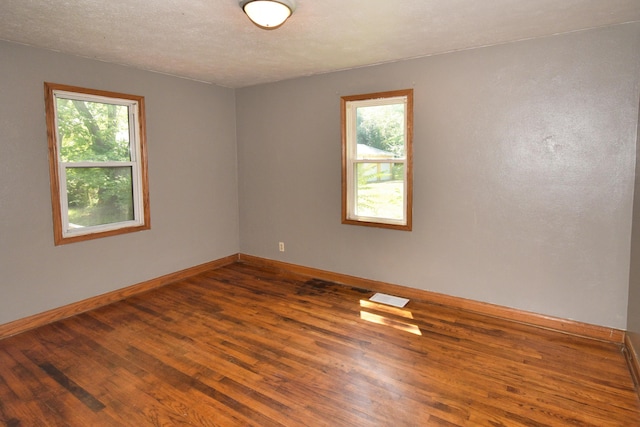 empty room featuring a wealth of natural light, visible vents, baseboards, and hardwood / wood-style floors