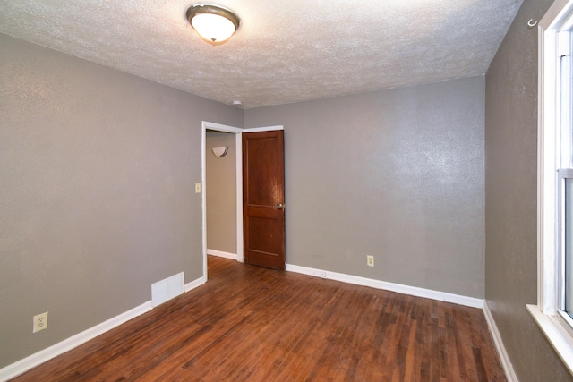 spare room featuring visible vents, a textured ceiling, baseboards, and wood finished floors