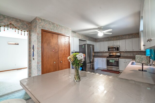 kitchen with white cabinets, stainless steel appliances, a sink, wallpapered walls, and a ceiling fan