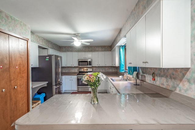 kitchen featuring stainless steel appliances, a peninsula, a sink, white cabinetry, and a ceiling fan