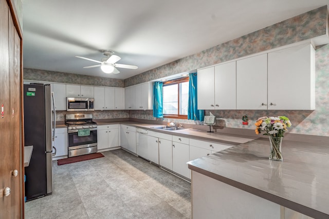kitchen featuring a ceiling fan, a sink, a peninsula, appliances with stainless steel finishes, and white cabinetry