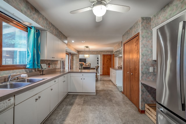 kitchen with a sink, white dishwasher, freestanding refrigerator, a peninsula, and white cabinetry