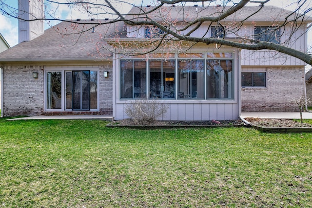 rear view of house featuring a sunroom, a yard, and brick siding