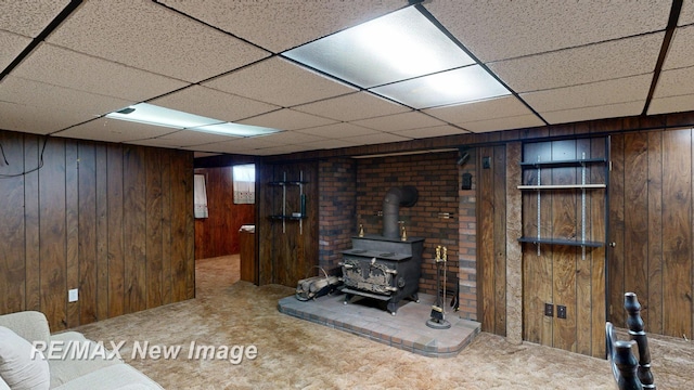 finished basement featuring wood walls, a wood stove, a drop ceiling, and carpet