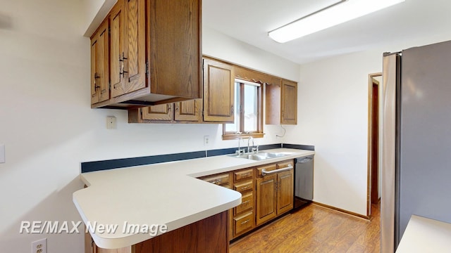 kitchen with dishwasher, a sink, light countertops, brown cabinetry, and light wood-style flooring