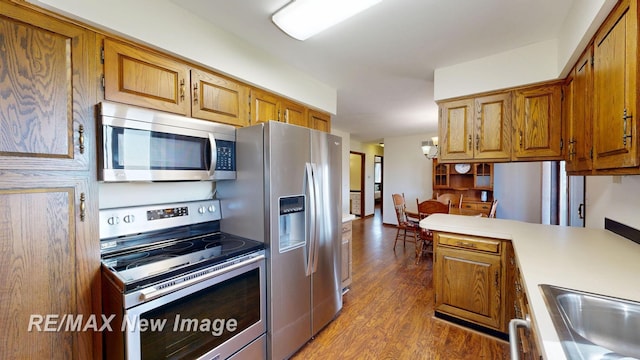 kitchen featuring a peninsula, light countertops, dark wood-type flooring, brown cabinetry, and stainless steel appliances
