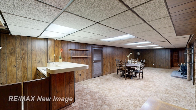 carpeted dining room featuring wooden walls, a drop ceiling, and bar area