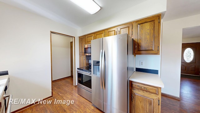 kitchen featuring baseboards, light countertops, appliances with stainless steel finishes, dark wood-style floors, and brown cabinetry