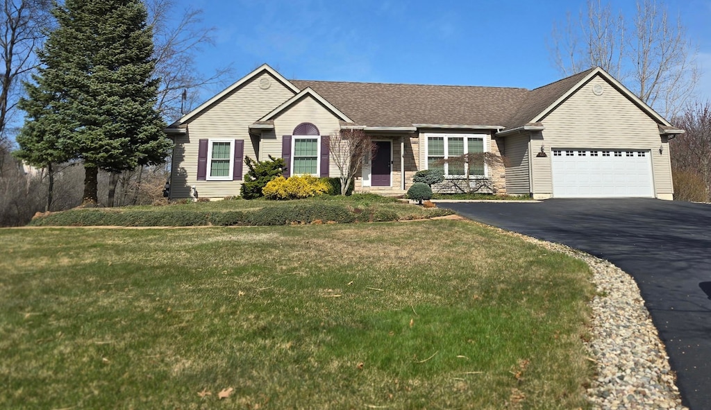 ranch-style home featuring an attached garage, driveway, a shingled roof, and a front lawn