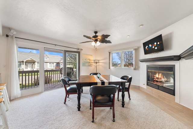 dining room featuring a glass covered fireplace, a healthy amount of sunlight, a ceiling fan, and a textured ceiling