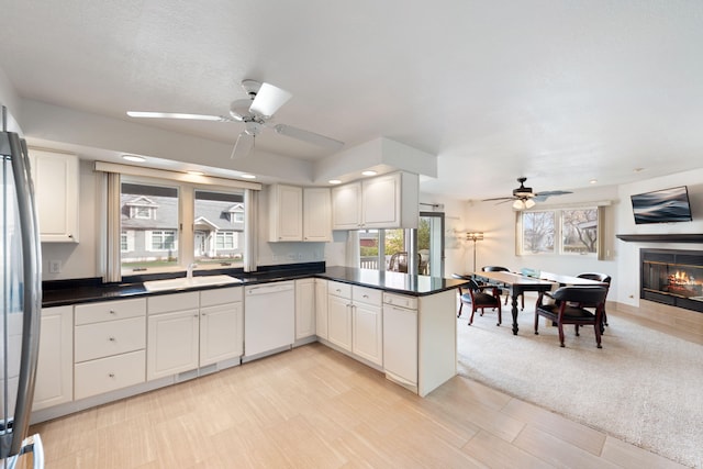 kitchen featuring dark countertops, a ceiling fan, a sink, a glass covered fireplace, and dishwasher