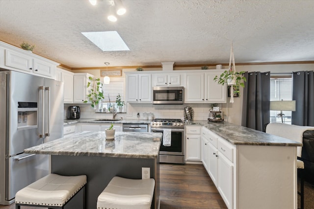 kitchen with a breakfast bar, a skylight, a textured ceiling, and appliances with stainless steel finishes