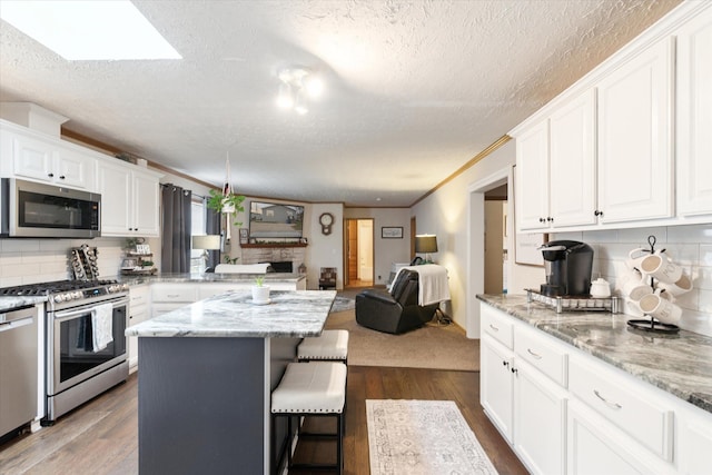 kitchen with a breakfast bar, open floor plan, a textured ceiling, white cabinets, and stainless steel appliances