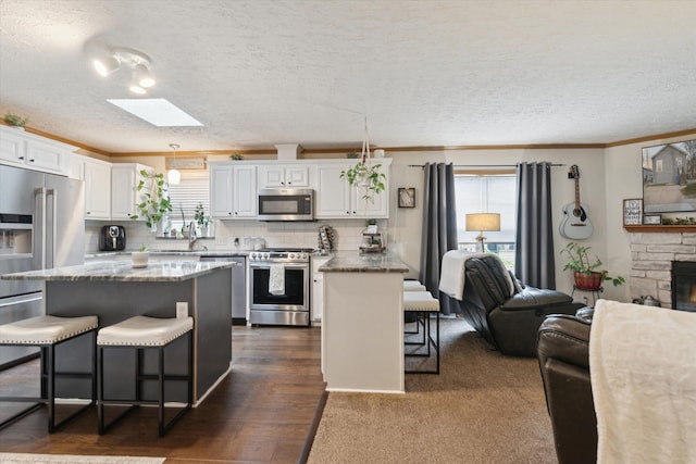 kitchen featuring white cabinetry, a skylight, stainless steel appliances, open floor plan, and a breakfast bar area