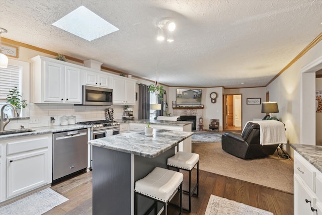 kitchen with white cabinets, a breakfast bar, appliances with stainless steel finishes, a sink, and open floor plan