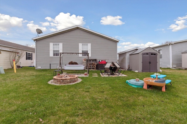 back of property featuring a yard, a storage unit, a fire pit, and an outdoor structure