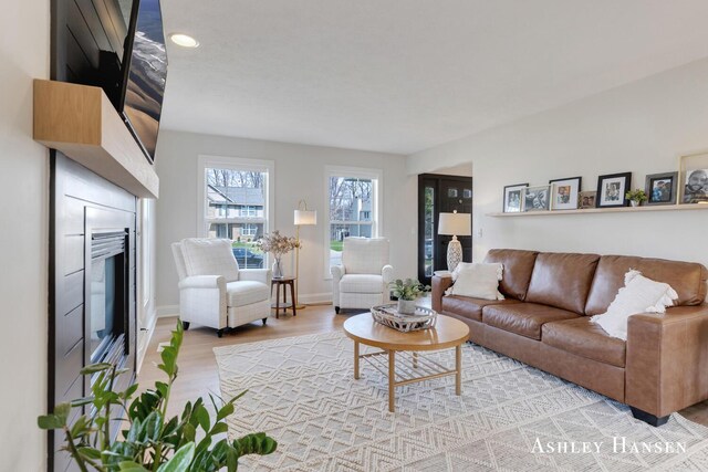 living area with a glass covered fireplace, recessed lighting, light wood finished floors, and baseboards
