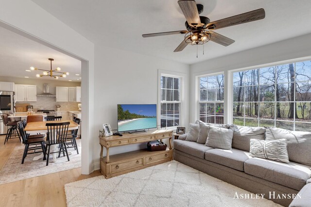 living room with light wood-type flooring and ceiling fan with notable chandelier