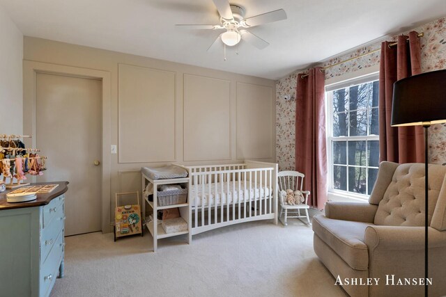 bedroom with light colored carpet, ceiling fan, and a nursery area