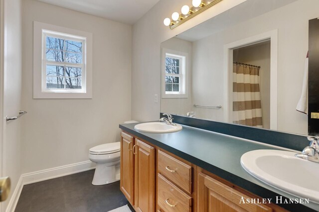 full bath with toilet, double vanity, a sink, and baseboards