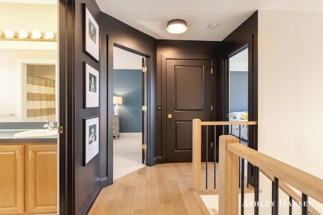 hall with baseboards, light wood-style floors, a sink, and an upstairs landing