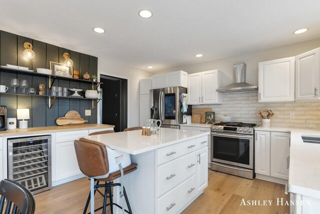 kitchen with wall chimney exhaust hood, white cabinetry, appliances with stainless steel finishes, light countertops, and wine cooler