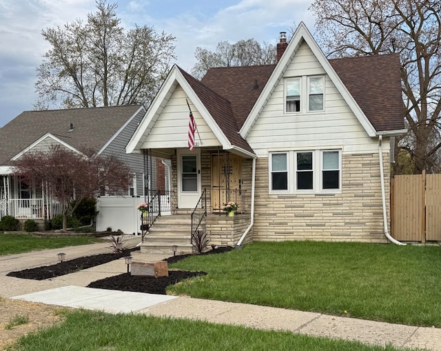 view of front of home with a chimney, fence, stone siding, a front yard, and roof with shingles