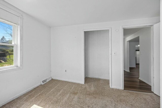 unfurnished bedroom featuring freestanding refrigerator, baseboards, carpet, and visible vents