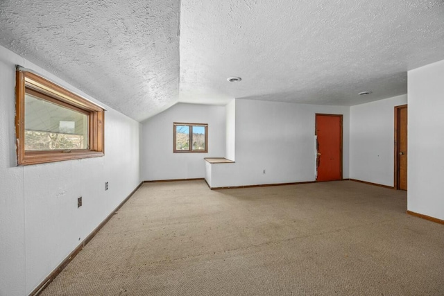 additional living space featuring a textured ceiling, visible vents, carpet floors, lofted ceiling, and baseboards