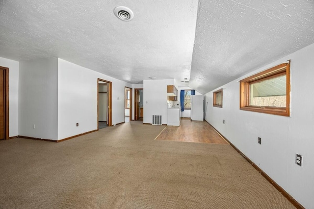 unfurnished living room with washer / clothes dryer, visible vents, a wealth of natural light, a textured ceiling, and carpet floors