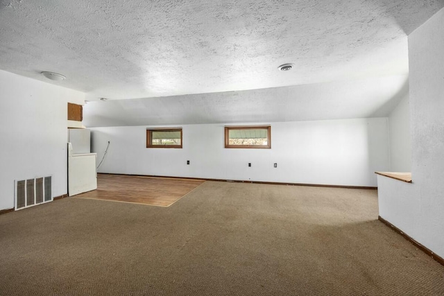 additional living space featuring a textured ceiling, baseboards, carpet, and visible vents