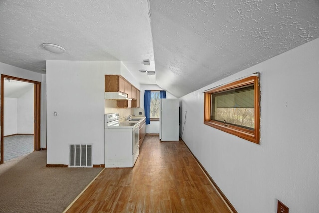 hallway with visible vents, baseboards, a textured ceiling, wood finished floors, and vaulted ceiling