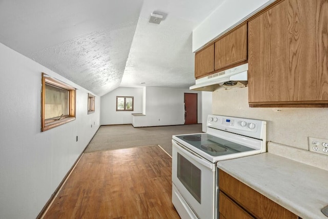 kitchen featuring light countertops, electric range, under cabinet range hood, brown cabinetry, and lofted ceiling